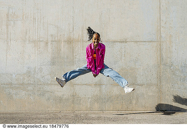 Happy dancer jumping in front of wall on sunny day
