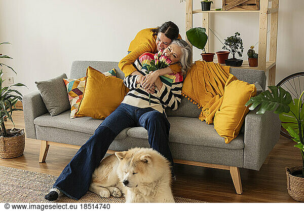 Happy daughter giving flowers and hugging mother at home