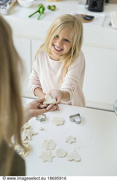 Happy daughter showing heart shape made from dough to mother at home