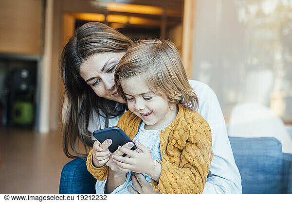 Happy daughter using smart phone with mother at home