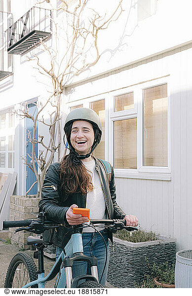Happy delivery person standing with smart phone and bicycle in front of building
