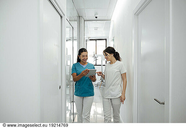 Happy dentist discussing with colleague over tablet PC in corridor