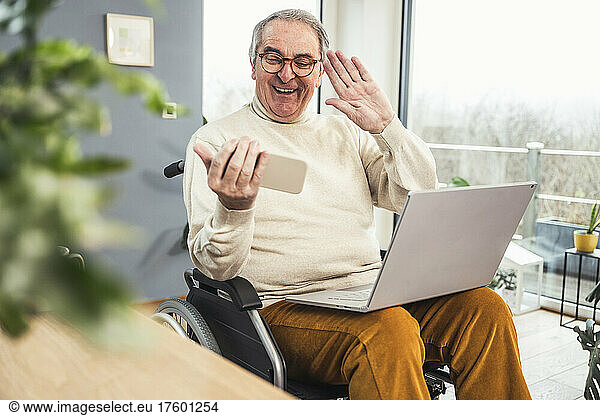 Happy disabled man waving hand on video call through smart phone at home