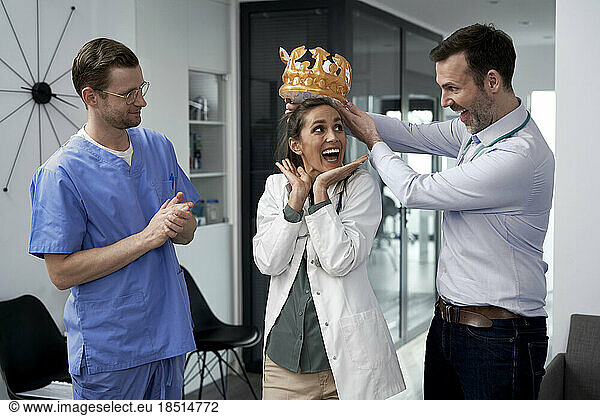 Happy doctor giving crown to colleague in clinic