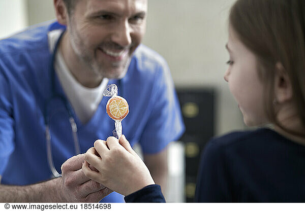 Happy doctor giving lollipop to girl in clinic