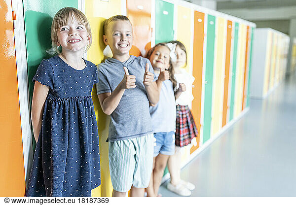 Happy elementary students standing near colorful lockers in school corridor