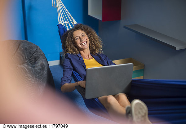 Happy employee with laptop relaxing in hammock