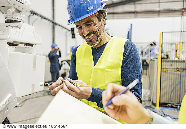 Happy engineer examining machine wire in industry