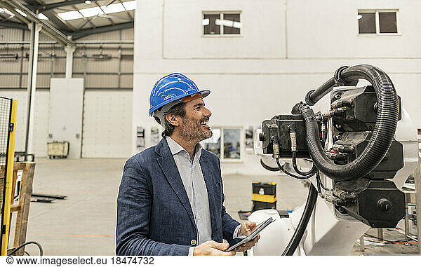 Happy engineer wearing hardhat looking at machine part in factory
