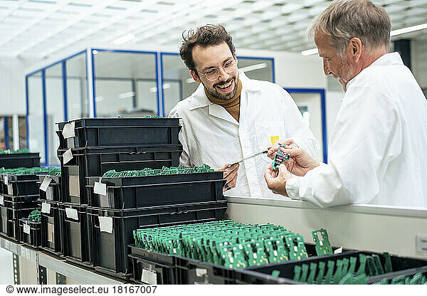 Happy engineer with colleague examining circuit board at industry
