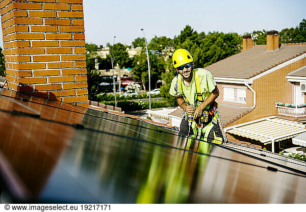 Happy engineer with drill machine installing solar panels on roof