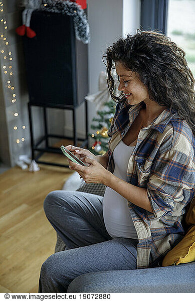 Happy expectant mother using smart phone at home