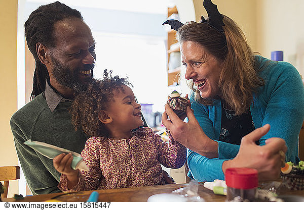 Happy family decorating Halloween cupcakes at table