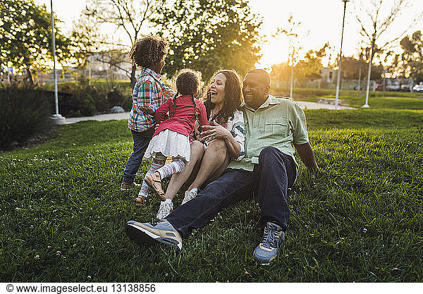 Happy family playing on grassy field at park during sunset