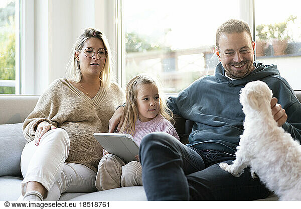 Happy family playing with dog sitting on sofa at home