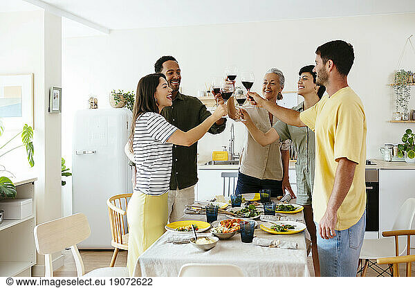Happy family raising toast standing near dining table in kitchen