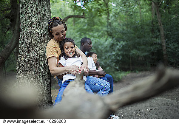 Happy family relaxing on fallen log on hike in woods