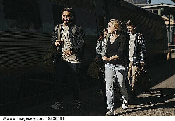 Happy family running towards train at railroad station during sunny day