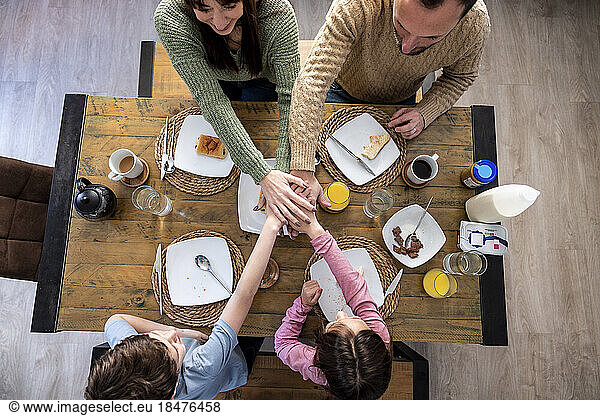 Happy family stacking hands together at table in kitchen