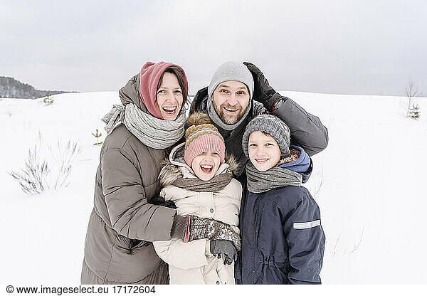 Happy family standing on snow covered land against sky during vacation
