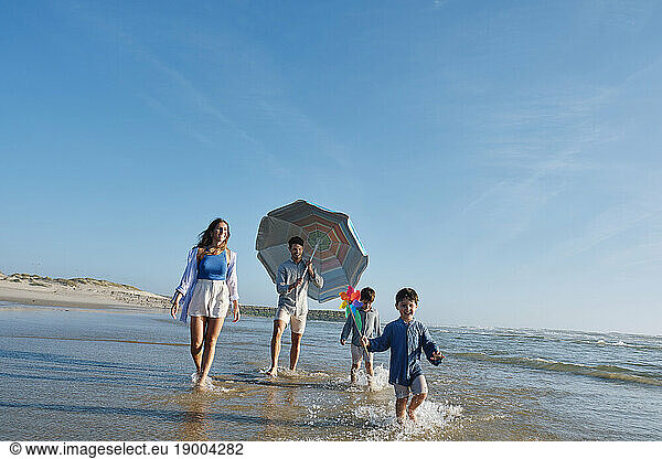 Happy family walking at beach on sunny day