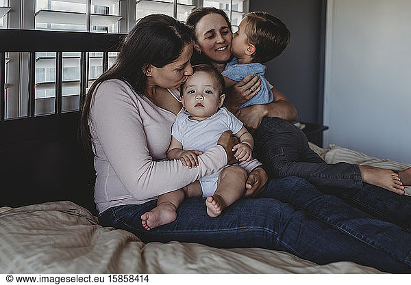 Happy family with two moms cuddling at home in bedroom