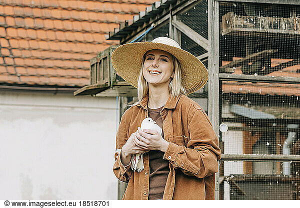 Happy farmer holding bird in front of dovecote