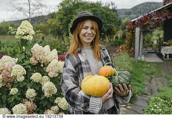 Happy farmer wearing hat holding pumpkins at farm