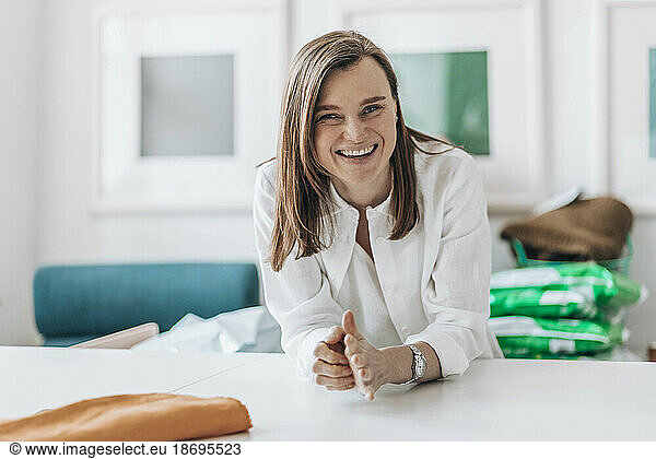 Happy fashion designer leaning on workbench
