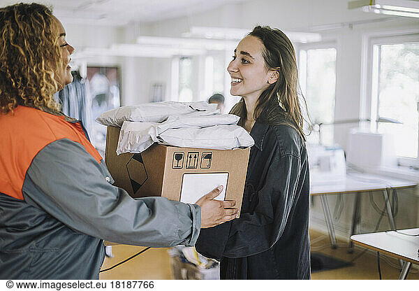 Happy fashion designer receiving package from female delivery person at workshop