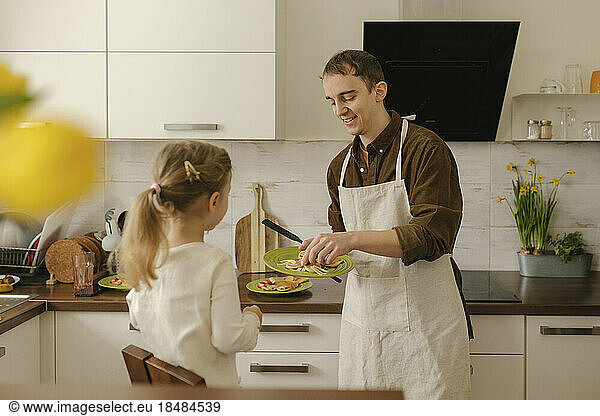 Happy father and daughter making pancakes in kitchen