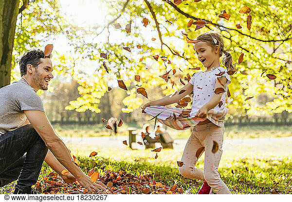 Happy father and daughter playing with autumn leaves in park