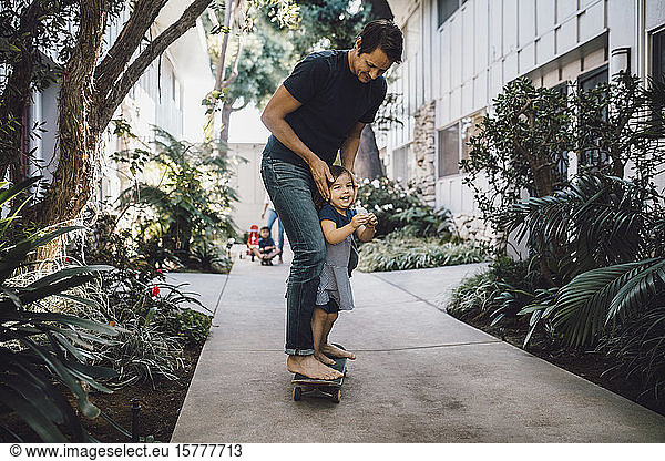 Happy father and daughter skateboarding on footpath