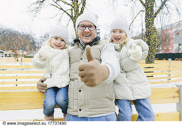 Happy father and daughters gesturing thumbs up at Christmas market