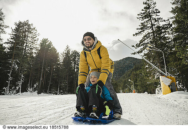 Happy father and son enjoys tobogganing on snow