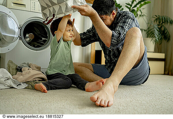 Happy father and son having fun with laundry basket and washing clothes in machine at home