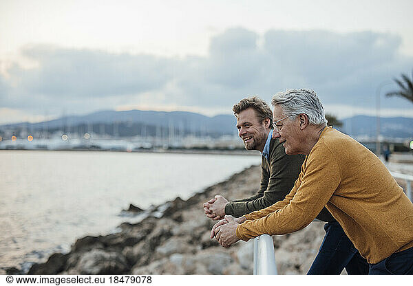 Happy father and son leaning on railing in front of sea
