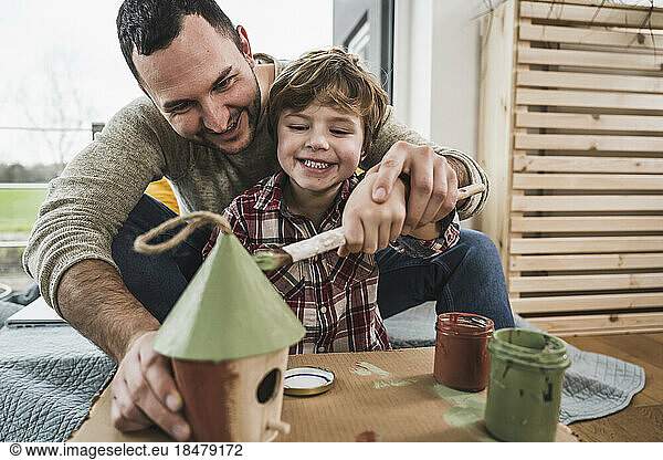 Happy father and son painting model house together at home