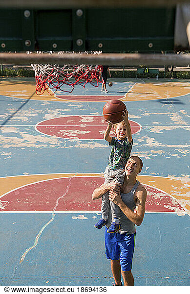 Happy father and son playing basketball at sports court