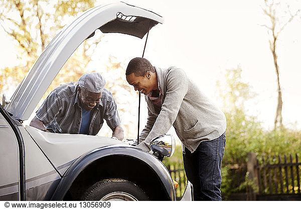 Happy father and son repairing car against sky