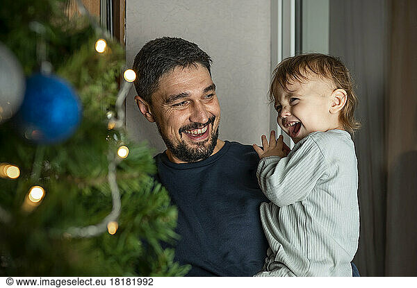Happy father carrying cute boy in front of Christmas tree at home
