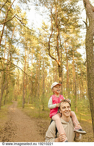 Happy father carrying daughter on shoulder and exploring forest