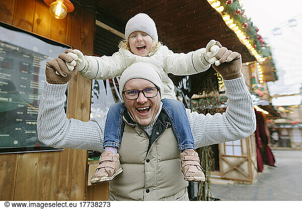 Happy father carrying daughter on shoulders at Christmas market