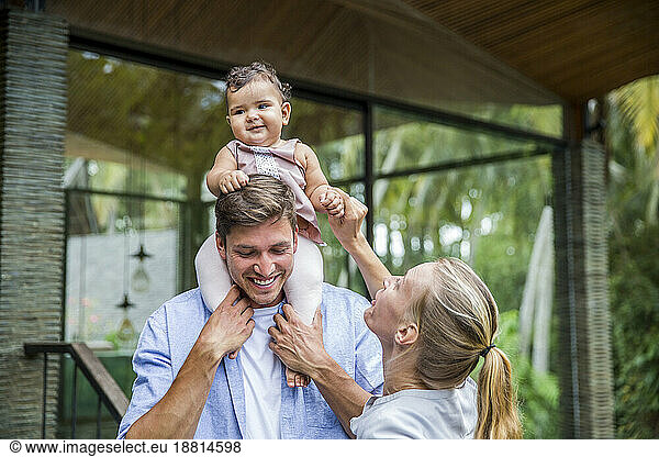Happy father carrying daughter on shoulders with mother holding hands