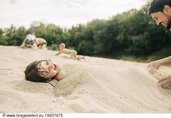 Happy father covering son with sand