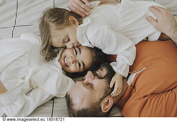 Happy father embracing cute daughters on bed at home