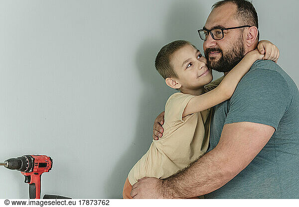 Happy father embracing son in front of wall