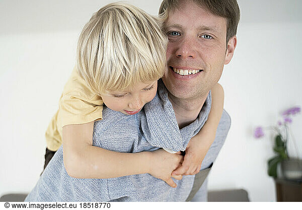 Happy father giving piggyback ride to son at home