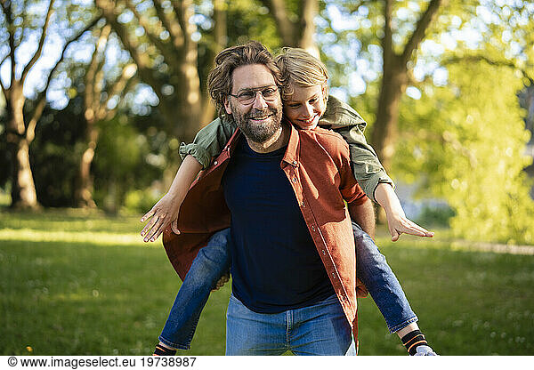 Happy father giving piggyback ride to son in park