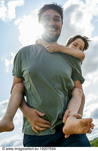 Happy father giving piggyback ride to son under cloudy sky
